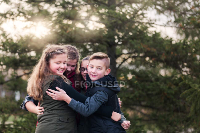 Retrato de niños y primos hembra abrazándose en el jardín - foto de stock