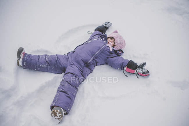Chica joven haciendo ángel de nieve en la nieve - foto de stock