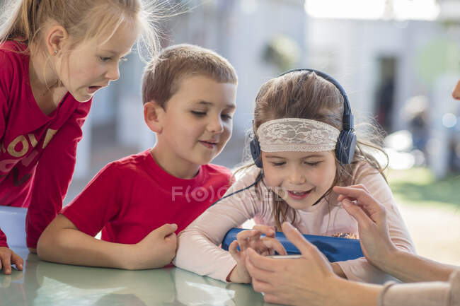 Young girl with friends, using smartphone, wearing headphones — Stock Photo