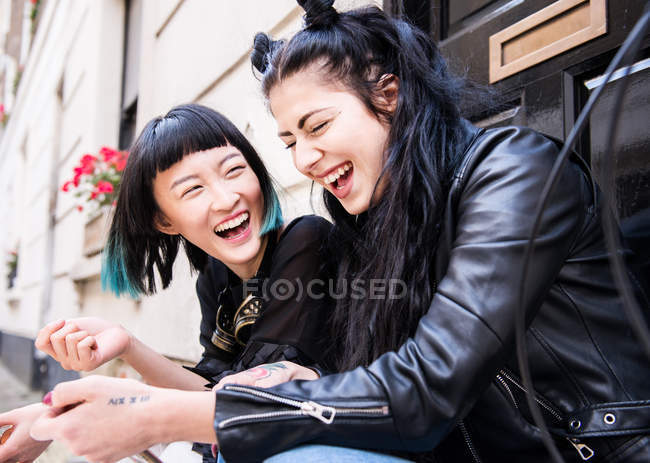 Two young stylish female laughing on doorstep — Stock Photo