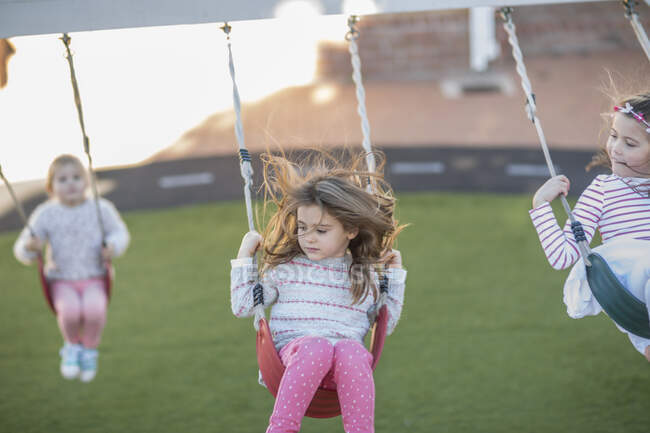 Ragazze alla scuola materna, oscillazione su altalene parco giochi in giardino — Foto stock