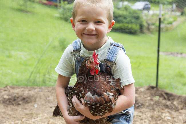 Boy holding speckled hen looking at camera smiling — Stock Photo