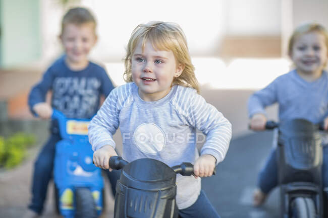 Девочки и мальчики в детском саду, гонки толкают мотоциклы в саду — стоковое фото