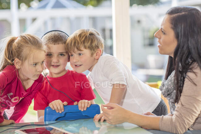 Mitte erwachsene Frau sitzt mit drei kleinen Kindern, kleiner Junge hält digitales Tablet, trägt Kopfhörer — Stockfoto