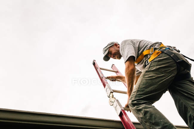 Workman outdoors, climbing ladder, low angle view — Stock Photo