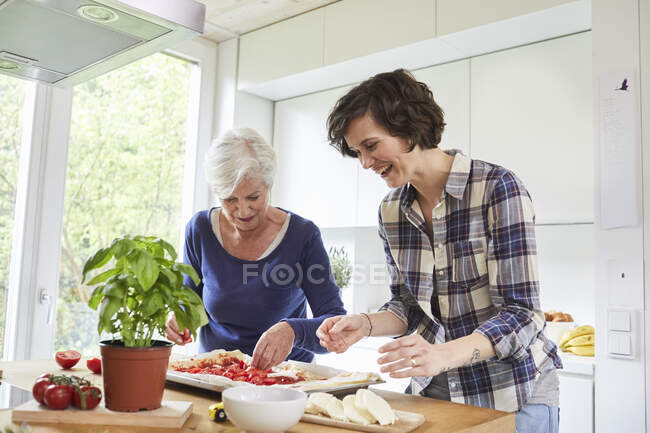 Madre e hija adulta en casa, preparando la comida juntas - foto de stock