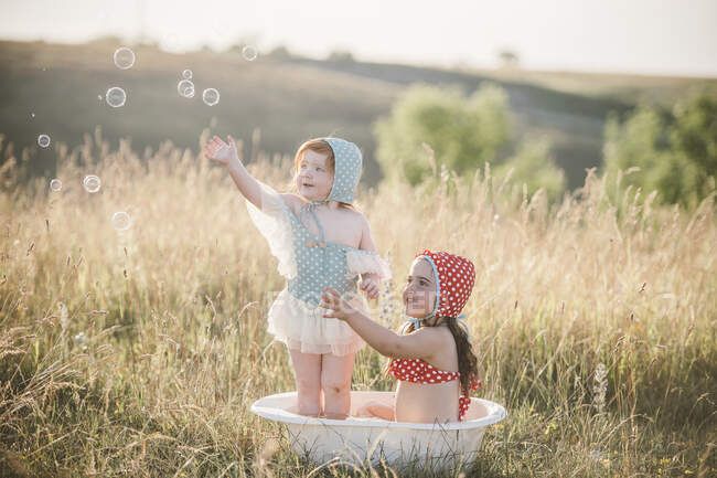 Две девушки в поле, играющие в пластиковой ванне с водой — стоковое фото