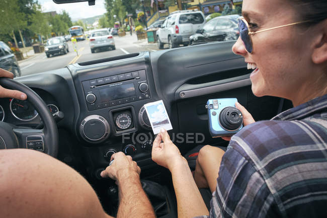 Over shoulder view of road trip couple driving and holding instant photograph, Breckenridge, Colorado, USA — Stock Photo