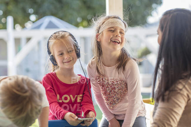 Young girl with friends, holding smartphone, wearing headphones — Stock Photo
