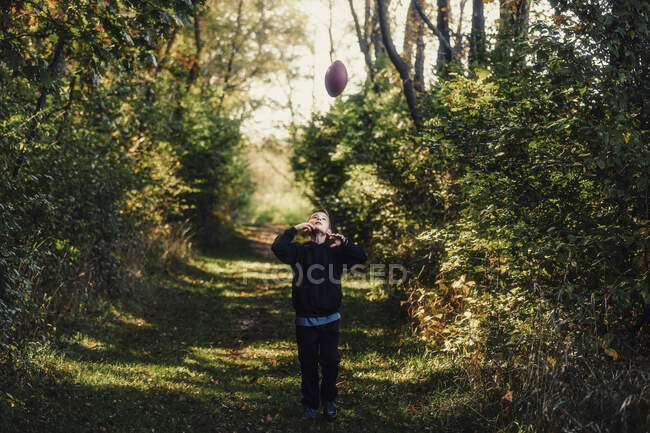 Jovem no cenário rural, jogando futebol americano no ar — Fotografia de Stock