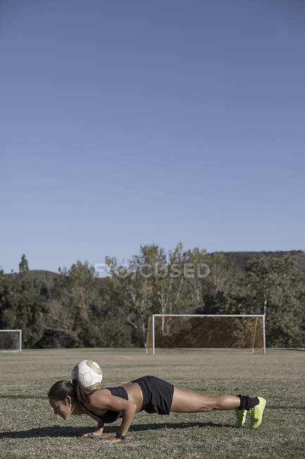 Mulher em campo de futebol fazendo flexões com futebol — Fotografia de Stock