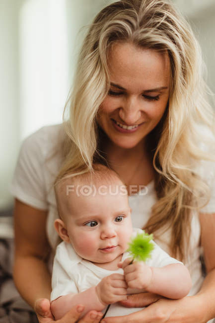 Bébé fille assis sur les genoux de la mère regardant la fleur — Photo de stock
