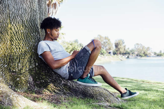 Homem sentado na raiz da árvore e usando smartphone — Fotografia de Stock