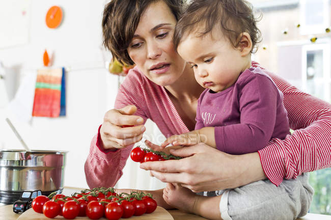 Mother and baby daughter in kitchen sorting tomatoes — Stock Photo