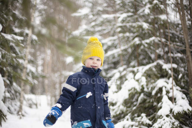 Retrato de niño en sombrero de punto amarillo caminando en el bosque de invierno - foto de stock