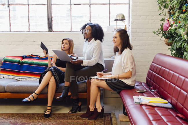 Seitenansicht von Kollegen, die mit Laptop zusammen auf dem Sofa im Büro sitzen — Stockfoto