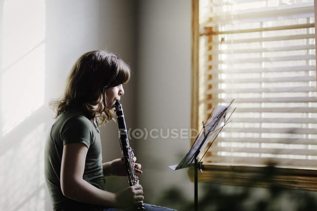 Дівчина з кларнетом і музикою стоїть практика за вікном — стокове фото