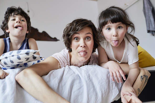 Портрет матери, сына и дочери, лежащих на кровати, выковыривающих язык — стоковое фото