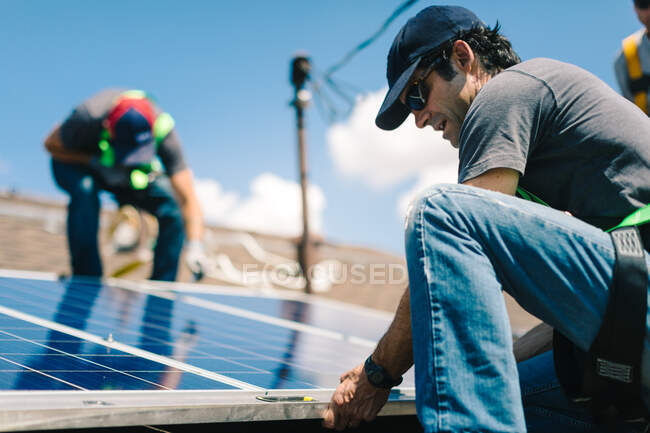 Drei Arbeiter installieren Sonnenkollektoren auf dem Dach des Hauses, niedriger Blickwinkel — Stockfoto