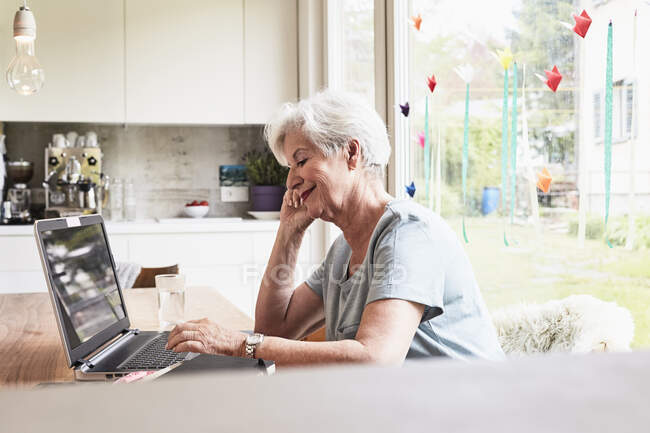 Старша жінка сидить за столом, використовуючи ноутбук — стокове фото
