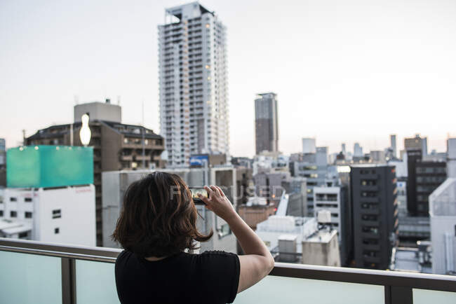 Femme prenant des photos du coucher du soleil depuis le balcon, Osaka, Japon — Photo de stock