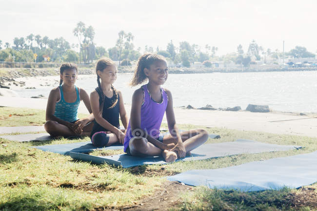 Trois écolières pratiquant la pose de yoga sur le terrain de sport scolaire — Photo de stock