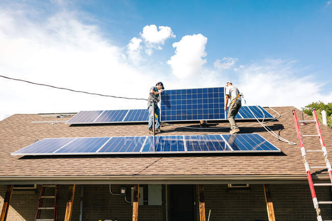 Dos trabajadores instalando paneles solares en el techo de la casa, vista de ángulo bajo - foto de stock