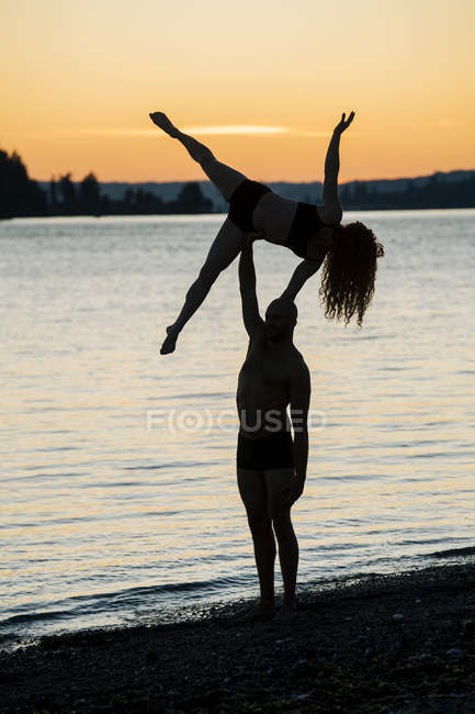 Пара практикующих йогу на пляже на закате — стоковое фото