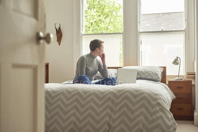 Woman with laptop, daydreaming on bed — Stock Photo