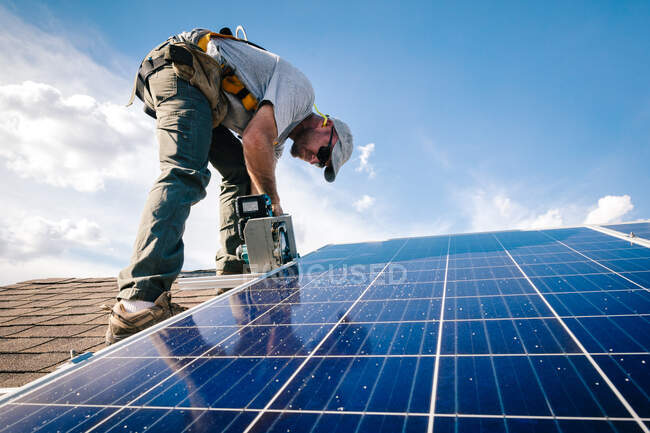 Workman installing solar panels on roof of house, low angle view — Stock Photo