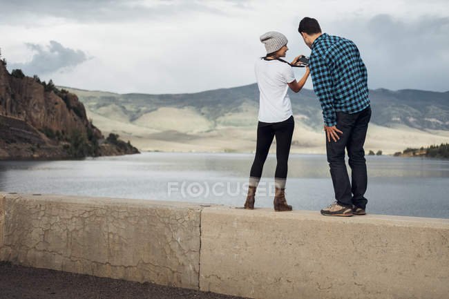 Пара, стоящая на стене рядом с водохранилищем Диллон, смотрит на камеру, вид сзади, Силверторн, Колорадо, США — стоковое фото