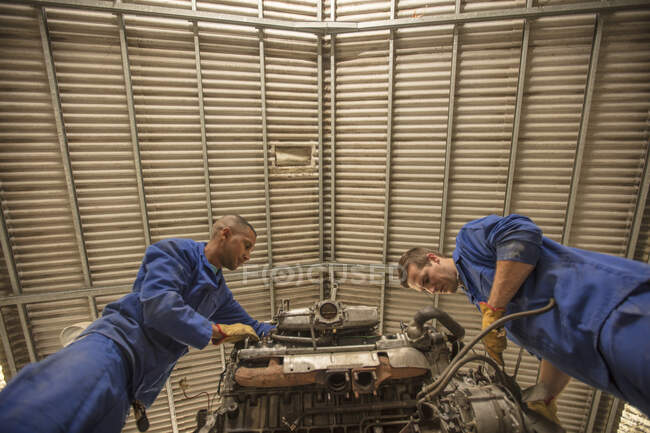 Vista de ángulo bajo de los mecánicos del coche que inspeccionan el motor del coche en el garaje de reparación - foto de stock