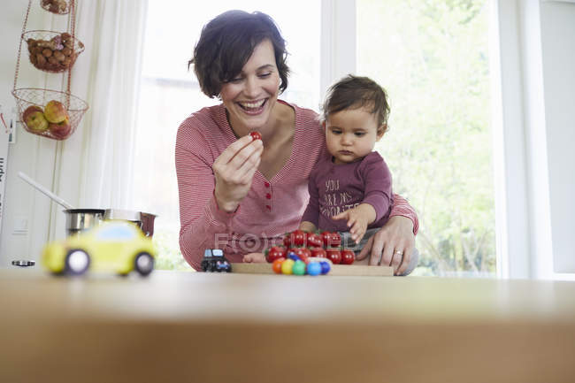Mother with baby girl at kitchen counter holding tomatoes — Stock Photo