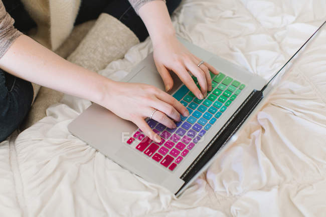 Mani donna digitando sul computer portatile sul letto — Foto stock