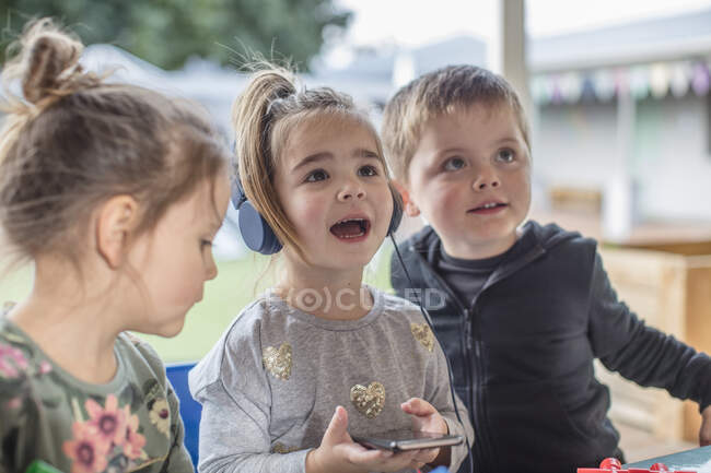 Young girl with friends, using smartphone, wearing headphones — Stock Photo
