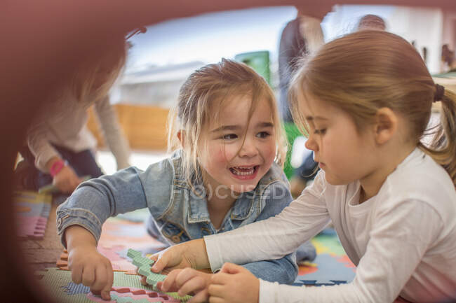 Two young girls, outdoors, playing with foam jigsaw pieces — Stock Photo