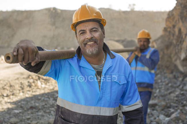 Portrait of quarry workers in quarry, carrying metal pipe — Stock Photo