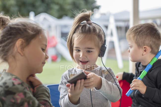 Menina com amigo, segurando smartphone, usando fones de ouvido — Fotografia de Stock