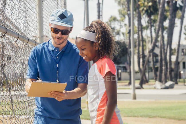 Teacher with clipboard talking to teenage schoolgirl soccer player on school sports field — Stock Photo