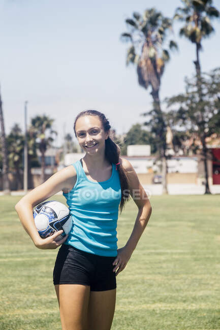 Портрет школьницы футболистки, держащей футбольный мяч на школьной спортивной площадке — стоковое фото