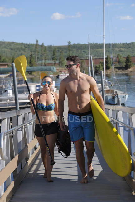 Paddleboarding couple carrying paddleboard on lake pier, Frisco, Colorado, USA — Stock Photo