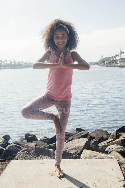 Retrato de colegiala practicando yoga pose en árbol junto al lago - foto de stock