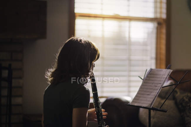 Fille avec support de musique jouant sur clarinette par fenêtre — Photo de stock