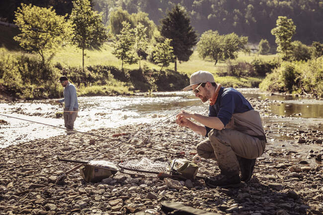 Joven pescador agachado con caña de pescar por río, Mozirje, Brezovica, Eslovenia - foto de stock