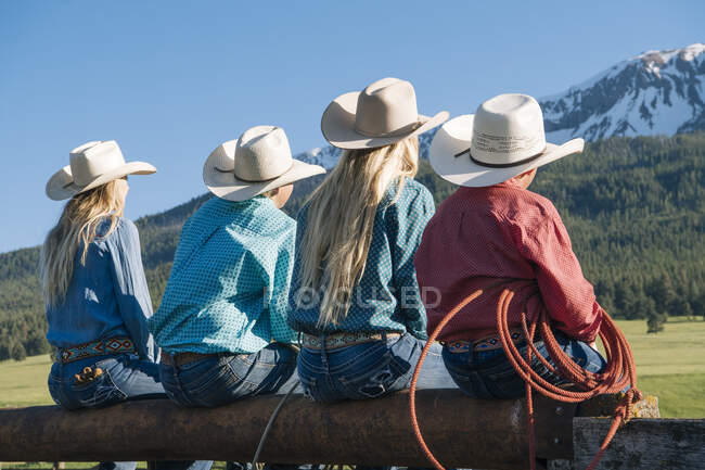 Vista trasera de los vaqueros y vaqueras en la cerca, mirando hacia otro lado, Enterprise, Oregon, Estados Unidos, América del Norte - foto de stock