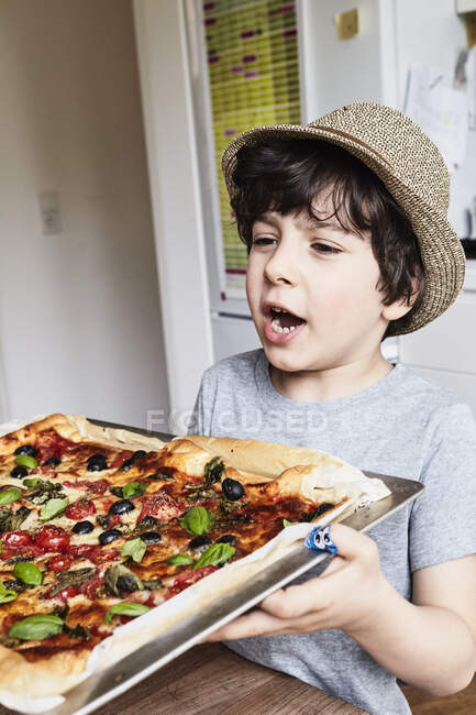 Young boy holding freshly baked pizza — Stock Photo