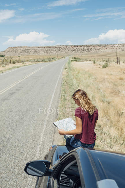 Frau sitzt auf Auto und schaut auf Landkarte — Stockfoto
