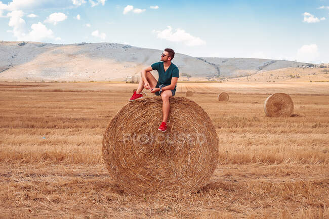 Man sitting on top of hay bale looking away — Stock Photo