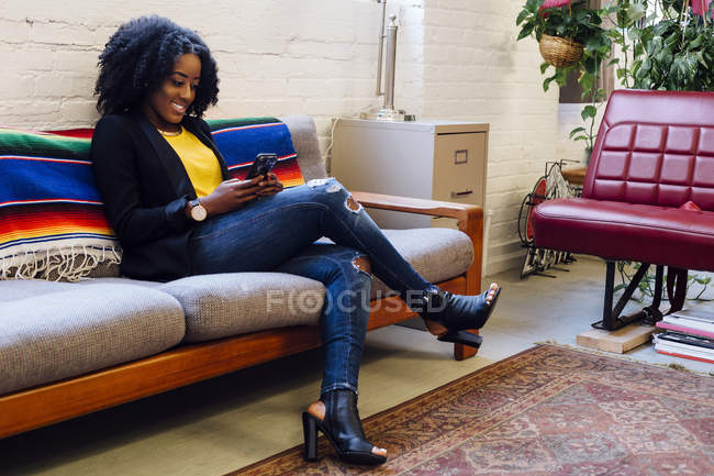 Женщина сидит на диване и смотрит на смартфон — стоковое фото