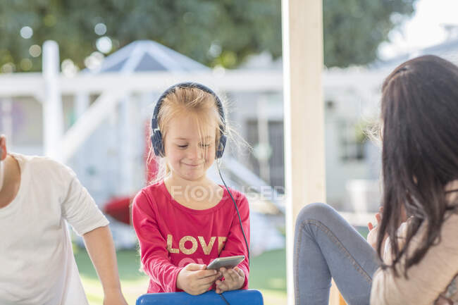 Jovencita sosteniendo teléfono inteligente, usando auriculares - foto de stock